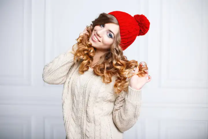 Junge glückliche schöne Frau in einem stilvollen Hut und modischen Strickpullover auf einem hellen Hintergrund