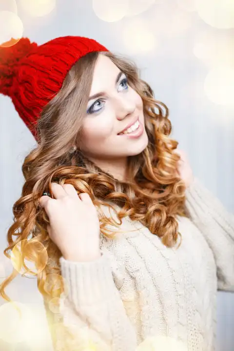 Glückliches junges Mädchen mit einem süßen Lächeln in einem warmen gestrickten Kleidungsstück auf einem Hintergrund aus goldenen Lichtern. Frohe Weihnachten