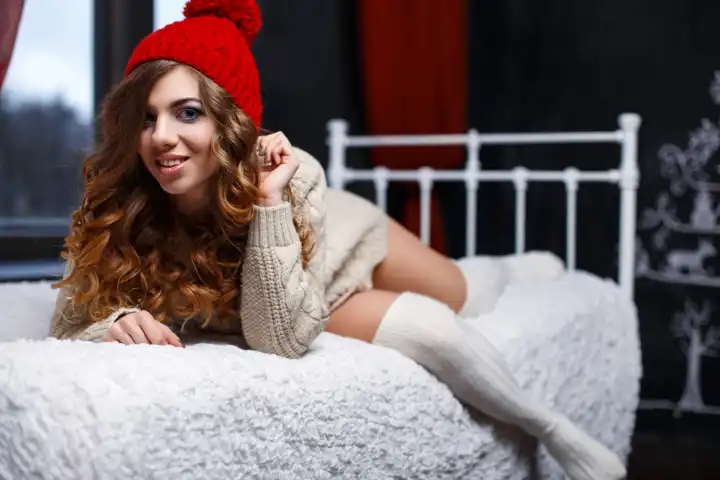 Hübsche Frau mit lockigem Haar in gestrickter warmer Kleidung auf dem Bett.