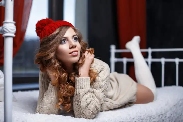 Young beautiful girl in stylish knitted sweater resting on the bed.