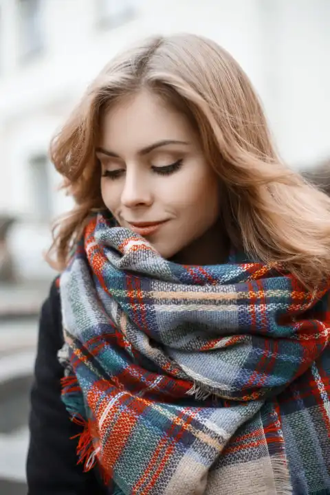 Cute young woman in trendy knitted scarf and black coat in autumn day