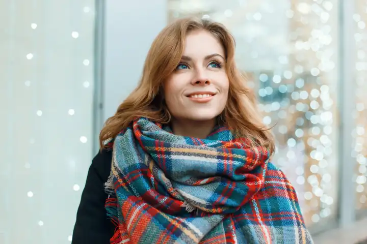 Süße Frau mit einem Lächeln in einem schönen stilvollen Schal auf dem Hintergrund der Lichter