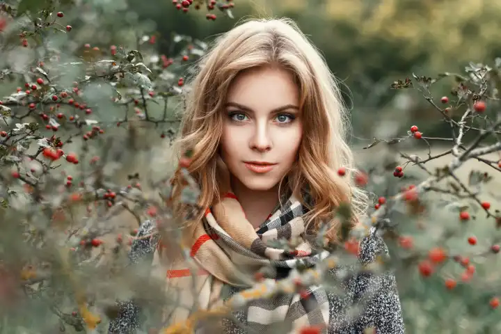 Schönes blondes Mädchen mit einem gestrickten Schal im Herbst Tag in der Nähe eines Baumes.