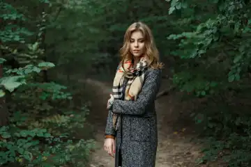 Schöne junge Frau in einem gestrickten Schal und Herbstmantel in der Nähe der grünen Blätter