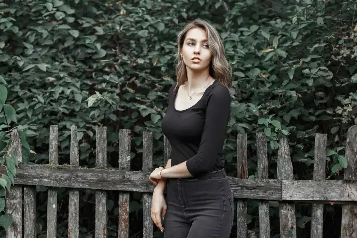 Schönes Mädchen in einem schwarzen T-Shirt in der Nähe des Holzzauns auf dem Hintergrund von Laub