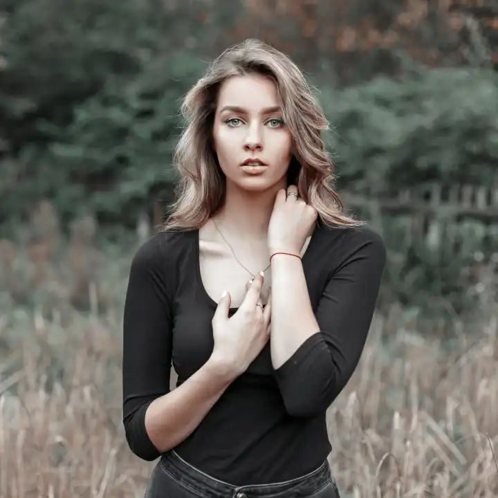Schönes junges blondes Mädchen in einem schwarzen T-Shirt in einem Feld in der Nähe von Bäumen