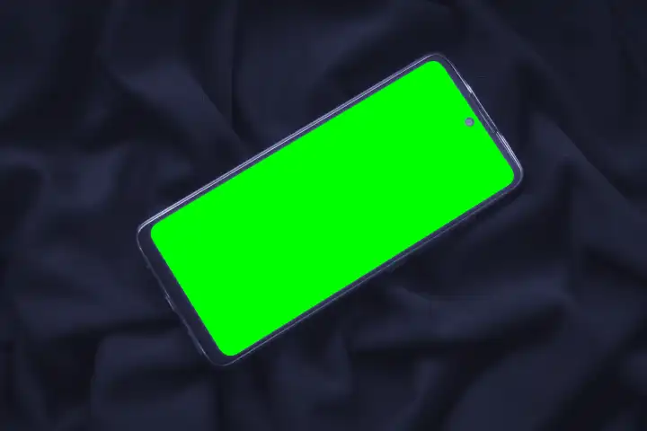 Smartphone mit grünem Bildschirm auf faltigem Stoff. Modernes Gerät auf modischem Textilhintergrund. Kopierbereich für die Platzierung von Bildern.
