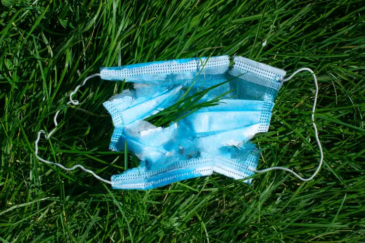 Gebrauchte medizinische Einweg-Gesichtsmaske mit Löchern auf grünem Gras. Modernes Müllkonzept.
