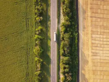 Top-down-Luftaufnahme auf Asphaltstraße mit LKW zwischen zwei landwirtschaftlichen Feldern