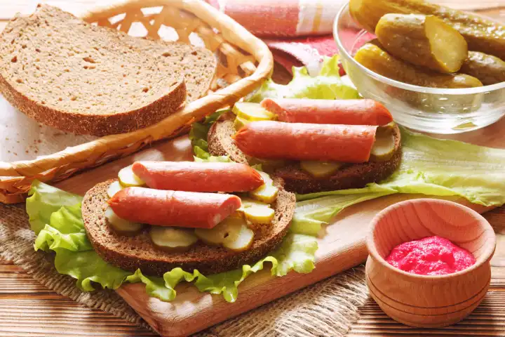 Homemade sandwiches with sliced smoked sausages and canned cucumber pickles. The cold appetizer with dark bread and spicy horseradish sauce.
