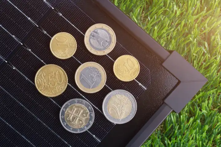 Das Konzept der Kosten für die Solarenergieerzeugung in Europa. Die Euro-Münzen auf dem elektrischen Solarpanel auf dem grünen Gras.