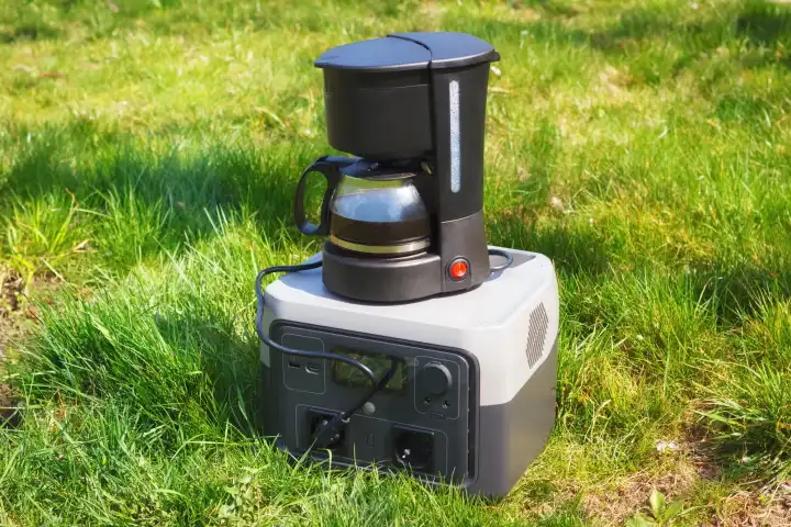 The portable set with power station and electric coffee maker on the green grass. The ground coffee cooking outdoors or during the blackout.
