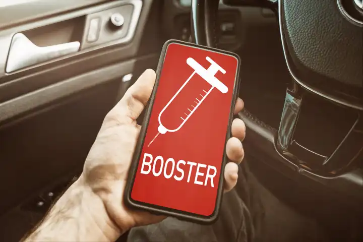 Smartphone cell phone labeled booster vaccination, one hand holding a digital notice for booster vaccination - PHOTOMONTAGE