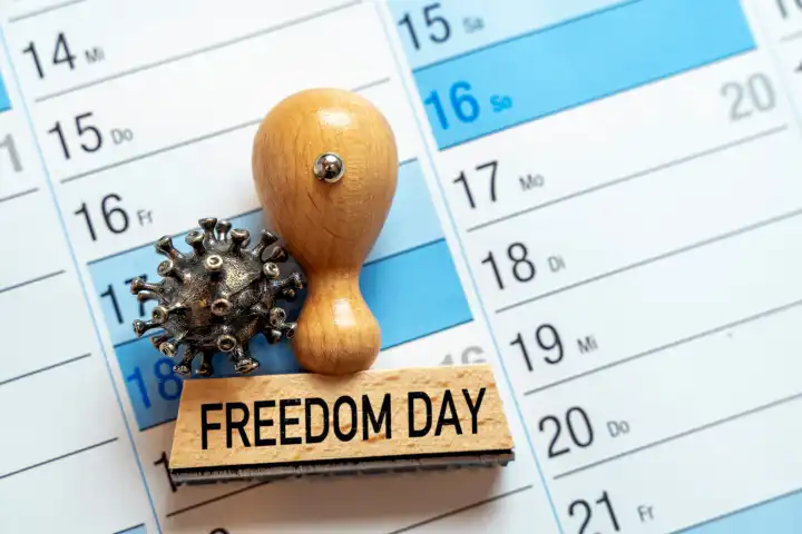 Stempel aus Holz mit der Aufschrift Freedom Day, Tag der Freiheit und Ende der Covid-19 Schutzmaßnahmen auf einem Kalender FOTOMONTAGE