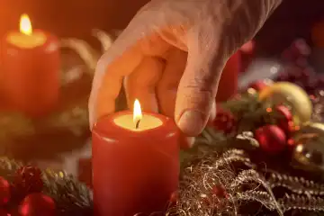 Hand an brennender Kerze auf einem Adventskranz. Symbolbild Weihnachten und Advent. FOTOMONTAGE
