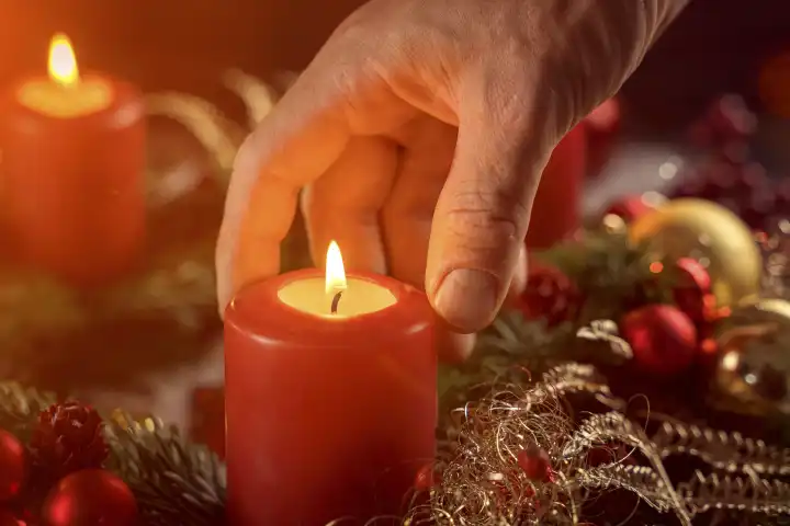 Hand an brennender Kerze auf einem Adventskranz. Symbolbild Weihnachten und Advent. FOTOMONTAGE
