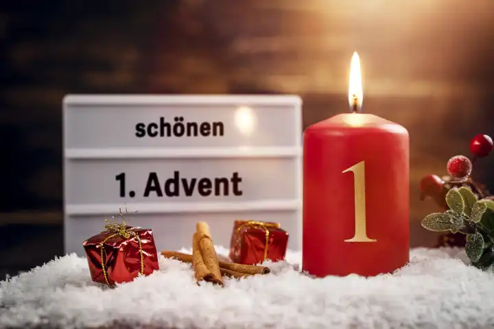 Eine Kerze brennt am ersten Advents Sonntag im Schnee mit einer Tafel und der Aufschrift: schönen 1 Advent FOTOMONTAGE