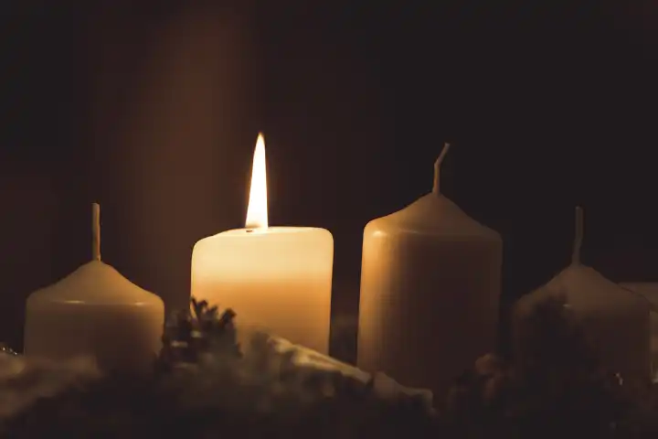 Die erste Kerze brennt auf einem Adventskranz am ersten Sonntag im Advent. Kerzenlicht, brennende Kerze an Weihnachten