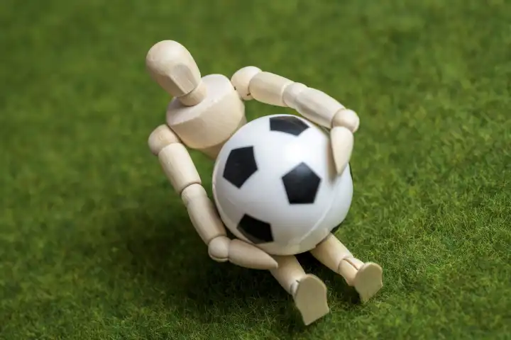 Eine Holzfigur mit einem Fußball auf einem Spielfeld. KI Künstliche Intelligenz beim Sport Konzept 