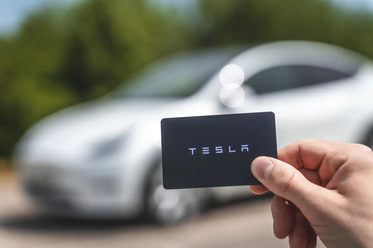 Hand hält eine TESLA Schlüsselkarte vor ein Model Y. Schlüsselkarte zum  aufsperren und zusperren eines Elektro Fahrzeuges der Marke Tesla -  CHROMORANGE