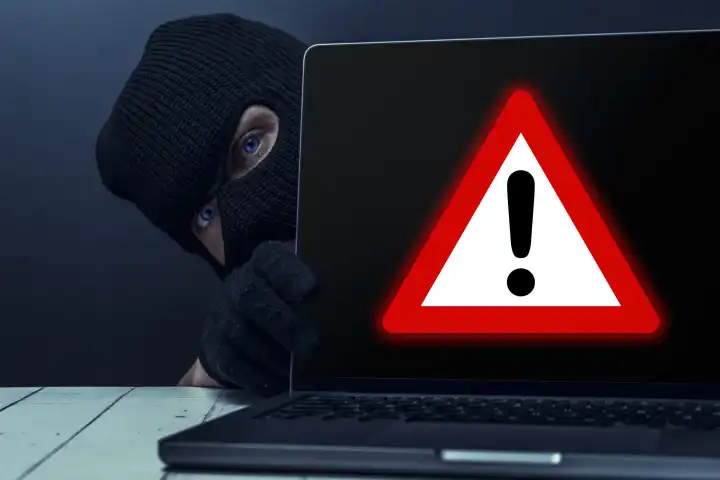 Warnung vor Betrug im Internet. Internetbetrug Konzept, Ein maskierter Mann hinter einem Laptop Computer mit einem Warnsymbol FOTOMONTAGE