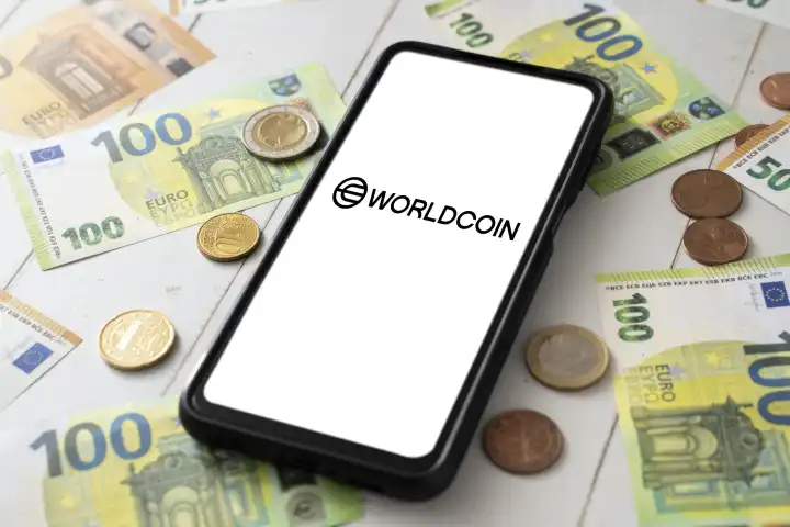 8 August 2023: Smartphone with Worldcoin logo on the screen next to Euro bills and coins. Cryptocurrency WDC PHOTOMONTAGE