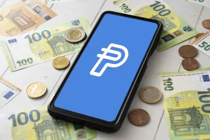8 August 2023: Smartphone with Paypal USD logo on screen next to Euro bills and coins. Cryptocurrency PYUSD from Paypal PHOTOMONTAGE