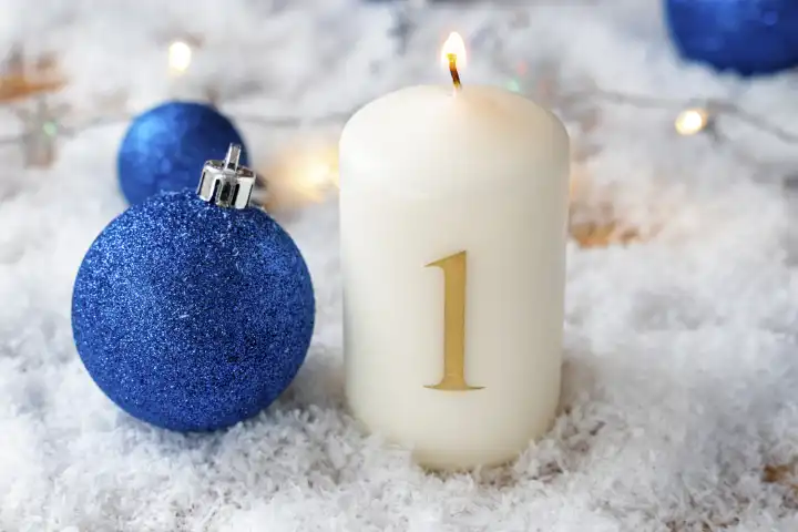 Erster Advent, brennende Kerze in Schnee mit blauen Christbaumkugeln. Kerze mit der Zahl 1