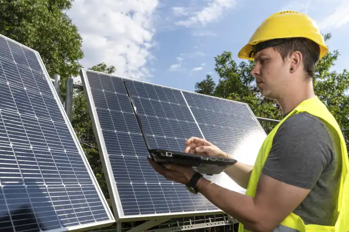 Bavaria, Germany - August 15, 2023: Engineer technician or electrician with a computer laptop in front of a freshly installed balcony power plant. Solar panels of a solar power plant (photovoltaic). Installation of green energy and electricity concept
