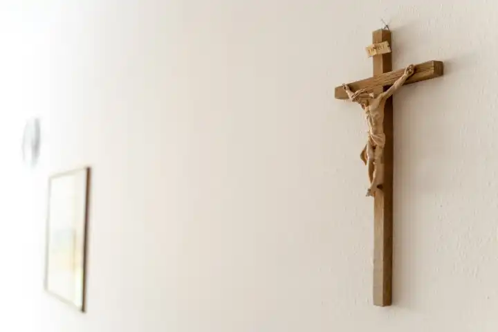 Ein christliches Kreuz aus Holz mit einer Jesus Figur und der Inschrift INRI hängt in einem Raum an einer weißen Wand