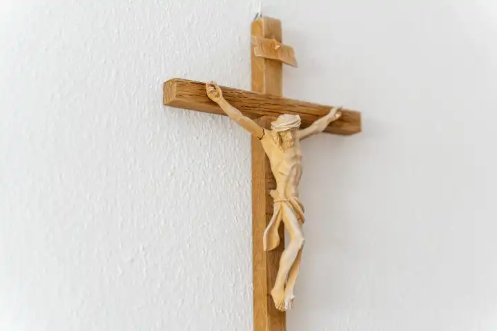 Ein christliches Kreuz aus Holz mit einer Jesus Figur und der Inschrift INRI hängt in einem Raum an einer weißen Wand