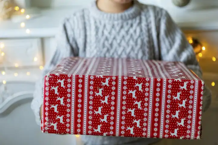 Ein Kind hält ein in weihnachtliches Geschenkpapier eingepacktes Geschenk. Weihnachtsgeschenk