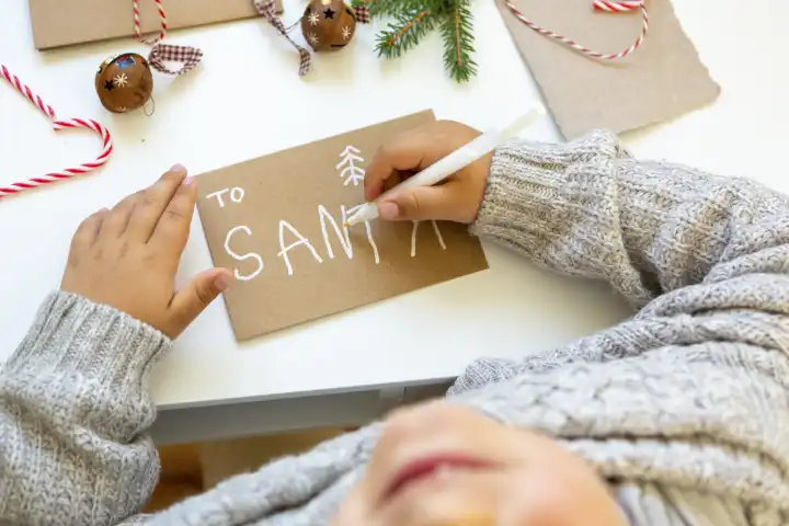 Ein Kind schreibt einem Brief an den Weihnachtsmann, Hände von einem jungen schreiben einen Brief mit einer Wunschliste für Weihnachten. Text: to Santa