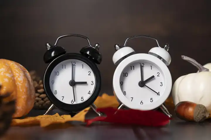 Bavaria, Germany - 19 August 2023: Symbol image time change. Alarm clock with winter time and summer time. White and black alarm clock in front of autumn decoration