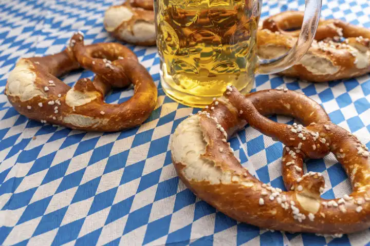 Bavaria, Germany - 25 August 2023: Oktoberfest themed photo, Bavarian flag with beer in Maßkrug and fresh brown pretzels. Bavarian tradition