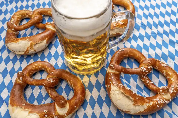Bavaria, Germany - 25 August 2023: Oktoberfest themed photo, Bavarian flag with beer in Maßkrug and fresh brown pretzels. Bavarian tradition