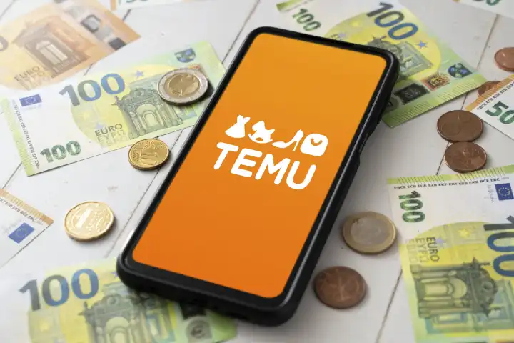 26 August 2023: TEMU Online Marketplace app on the screen of a smartphone. Cell phone with Temu logo next to euro banknotes PHOTOMONTAGE