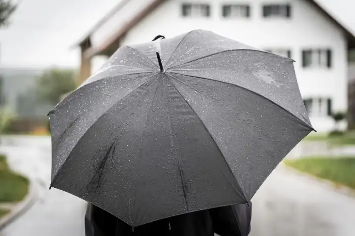 Kammlach, Bavaria, Germany - 27 August 2023: A man walking in rain through a village with an umbrella