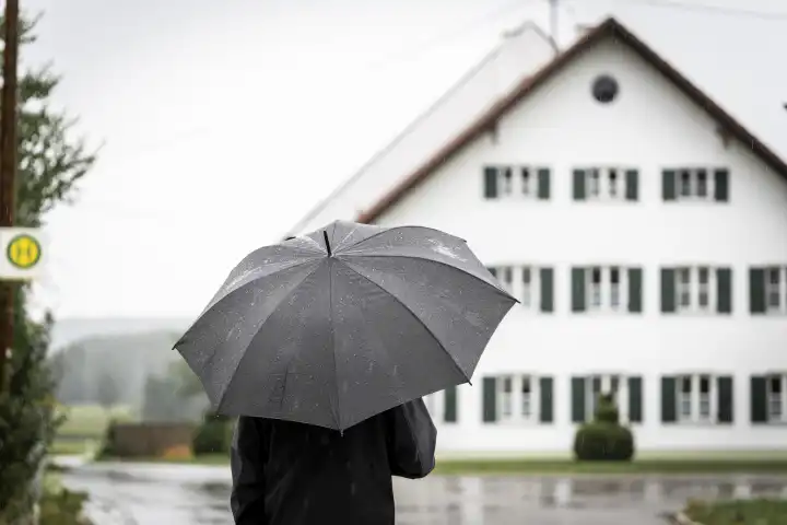 Ein Mann läuft spazieren bei Regen durch ein Dorf mit einem Regenschirm