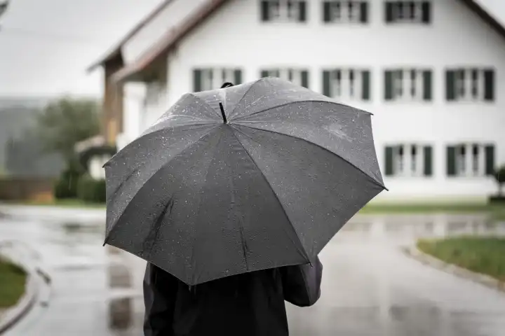 Ein Mann läuft spazieren bei Regen durch ein Dorf mit einem Regenschirm
