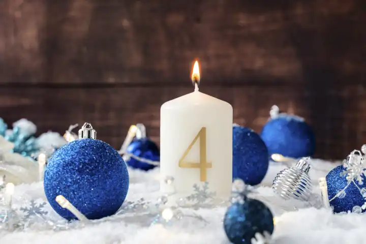 Der vierte Adventssonntag, eine weiße Kerze mit Aufschrift 4 brennt vor weihnachtlicher Dekoration mit blauen Christbaumkugeln. Vierter Advent