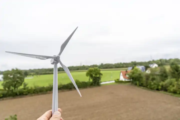 Bavaria, Germany - 29 August 2023: Hand holding a wind turbine in front of a rural field. Green energy concept through wind power