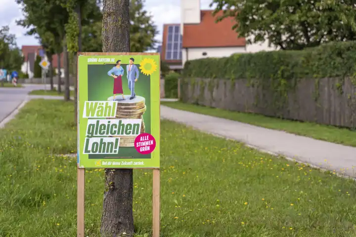 Ein Wahlplakat zur Landtagswahl in Bayern hängt an der Straße in einem Dorf. Die Partei die Grünen werben mit dem Slogan: Wähl gleichen Lohn!