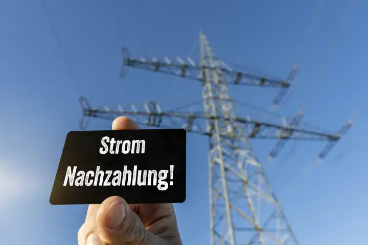 Hand hält Tafel vor einem Hochspannung Strommast mit der Aufschrift: Strom Nachzahlung FOTOMONTAGE