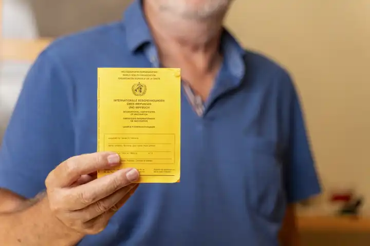 Ein alter Mann hält einen gelben Impfpass der WHO (Weltgesundheitsorganisation) in seiner Hand. Senior mit Impfbuch