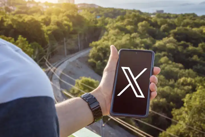 7 September 2023: Man holding smartphone with social media platform X on screen PHOTOMONTAGE