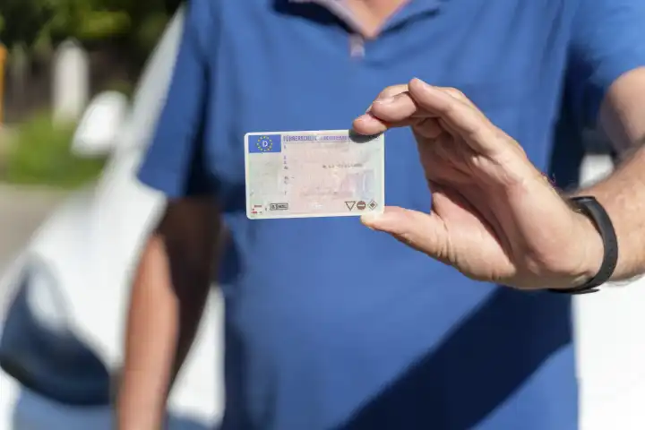 Ein alter Mann mit grauem Bart hält einen Führerschein der Bundesrepublik Deutschland in der Hand. Senior mit Fahrerlaubnis