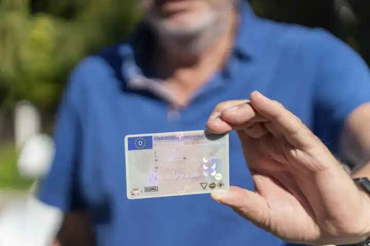 Ein alter Mann mit grauem Bart hält einen Führerschein der Bundesrepublik Deutschland in der Hand. Senior mit Fahrerlaubnis