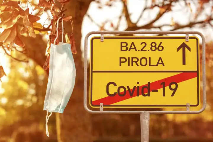 Schild mit Aufschrift Covid-19 durchgestrichen und Pfeil mit Schrift: BA.2.86 Pirola. Neue Corona Virus Variante. Schild neben Maske in einem Baum im Herbst FOTOMONTAGE