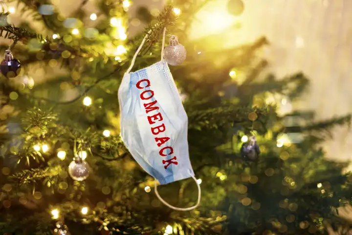 Corona Maske hängt an einem Weihnachtsbaum mit Aufschrift Comeback. Rückkehr der Pandemie Covid-19 FOTOMONTAGE